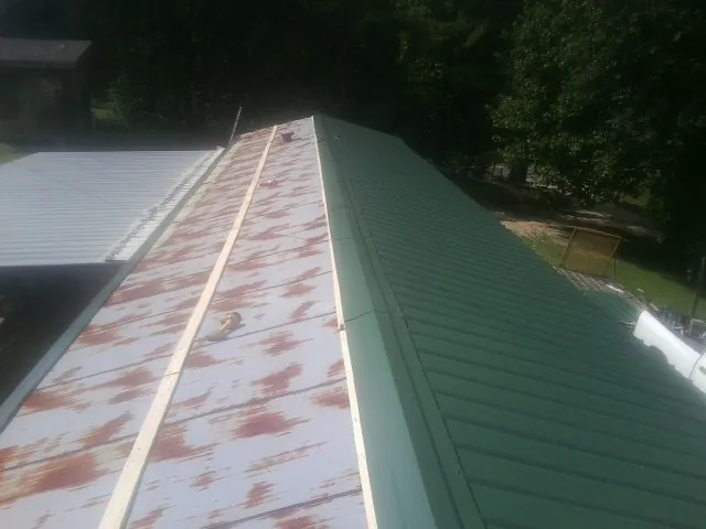 Old rusted panels beside newly installed green metal roofing — Wind Damage Roof Repair by Roofing Brothers in Benedict
